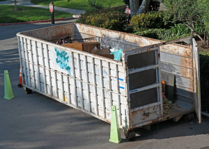 a white dumpster with one door open and lots of trash and furniture inside.